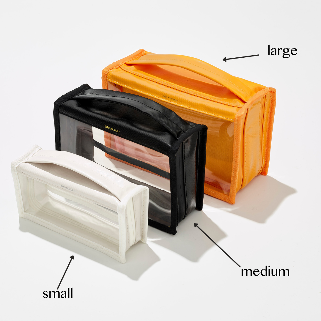 Product photograph of three take monday clear cosmetic bags in small white, medium black, and large bright orange sizes, all with transparent front panels and top handles displayed on a clean white background