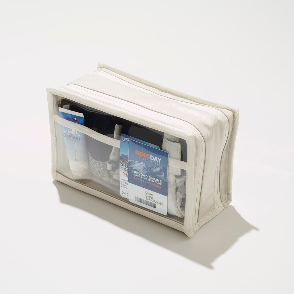 A white transparent travel pouch on a white surface contains a Belsun sunscreen tube an Epic Day ski lift ticket and a Paznaun ski pass in its clear pockets