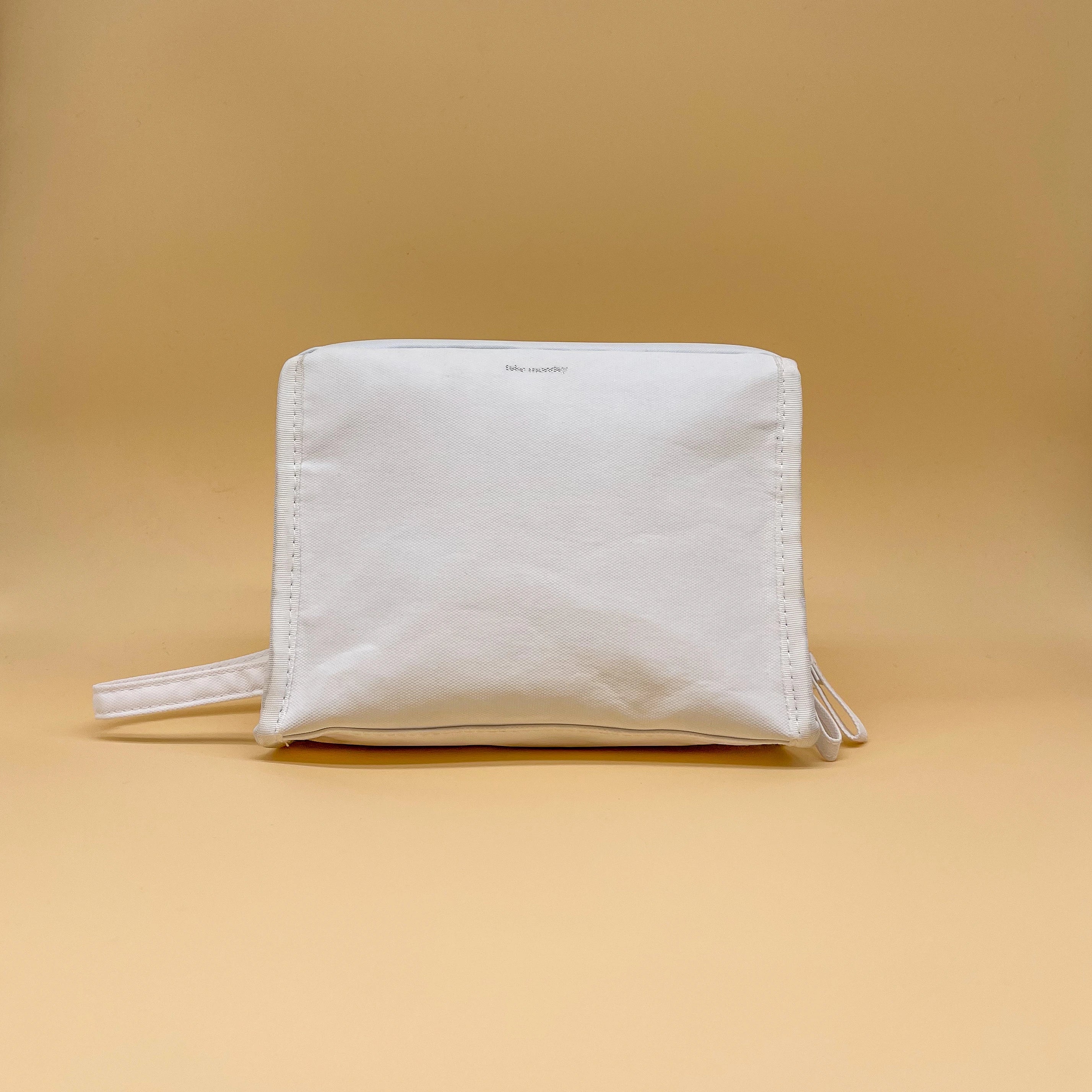 Baby Monsters white textured rectangular pouch featuring a subtle logo, prominent vertical stitching, and a side loop handle on a clean tan studio background